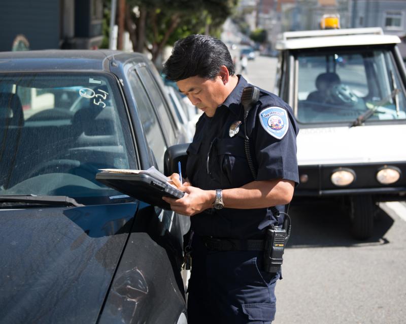 uniformed parking control officer writing ticket in front of abandoned vehicle