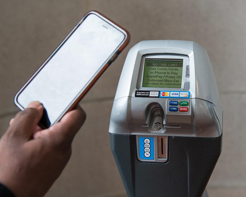 close up of parking meter with persons hand and phone