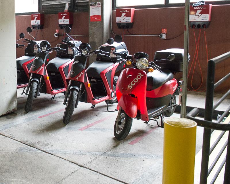 row of red electric rental scooters inside parking garage
