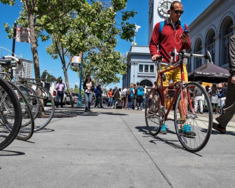 Man walks bicycle on the sidewalk in front of the Ferry Building