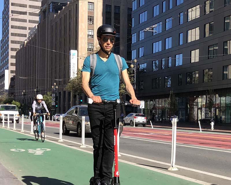 A person rides a scooter in a bike lane on Market Street, followed by a person riding a bike