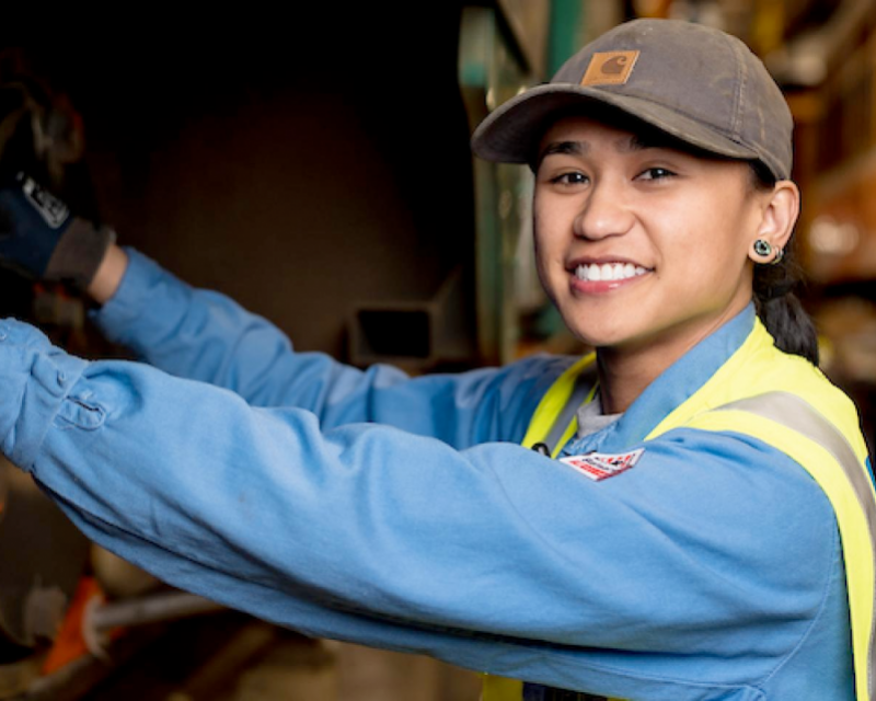 Jeena Villamor adjusts the track breaks for a historic streetcar. She smiles and wears a yellow safety vest.