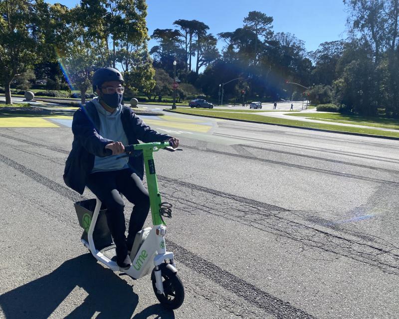 Person rides a lime green shared scooter through Golden Gate Park.