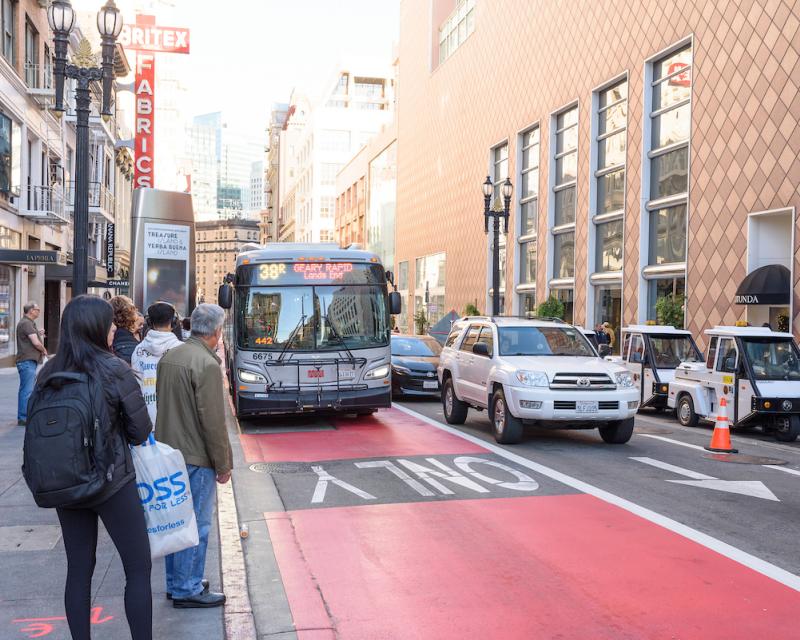 A 38R bus heads down a dedicated transit lane as passengers wait at a corner to board.