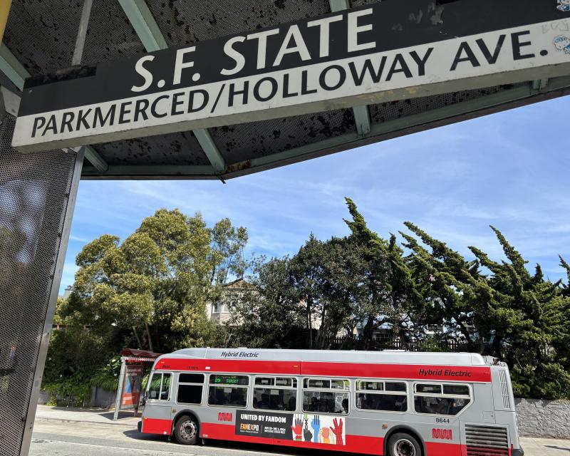 A Muni bus stops near a sign that says S.F. State.