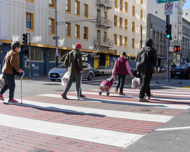 A group of people cross the street on a red and white striped crosswalk.