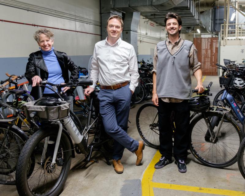 Three people stand near dozens of bikes in a bike storage area. 