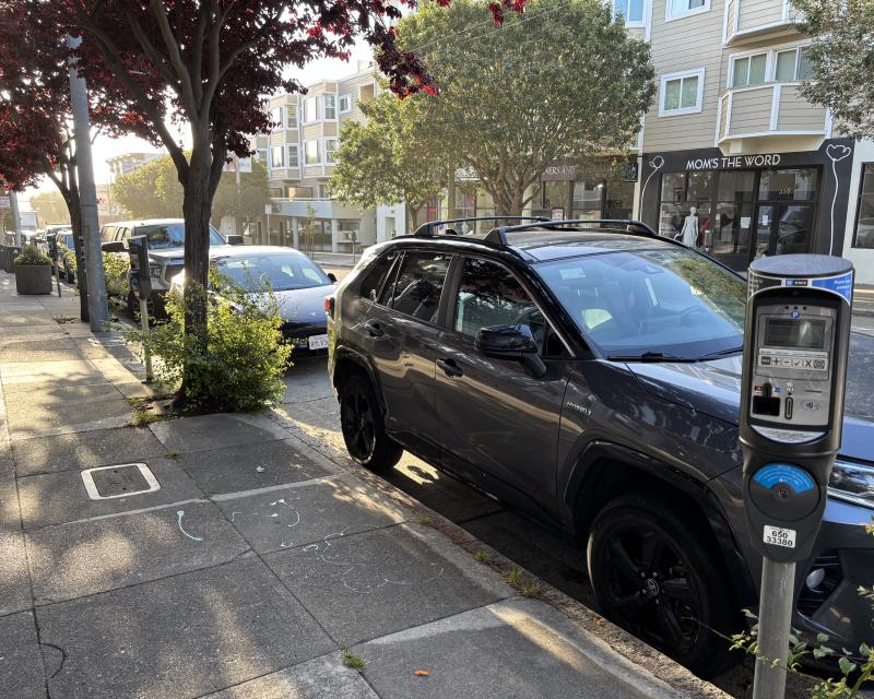 Cars parked on a street near the sidewalk and trees.