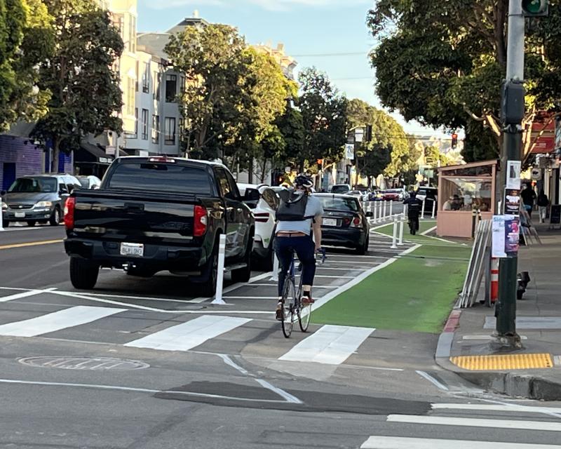 Person bikes toward a green side-running protected bikeway on Valencia Street.