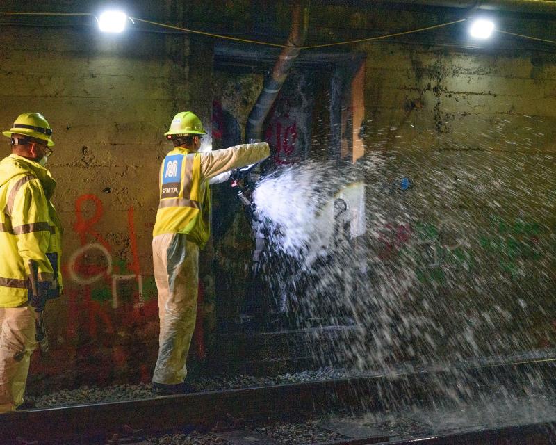 Two crew members wear yellow safety gear inside a Muni Metro tunnel as they flush standpipes for Fix-It Week.