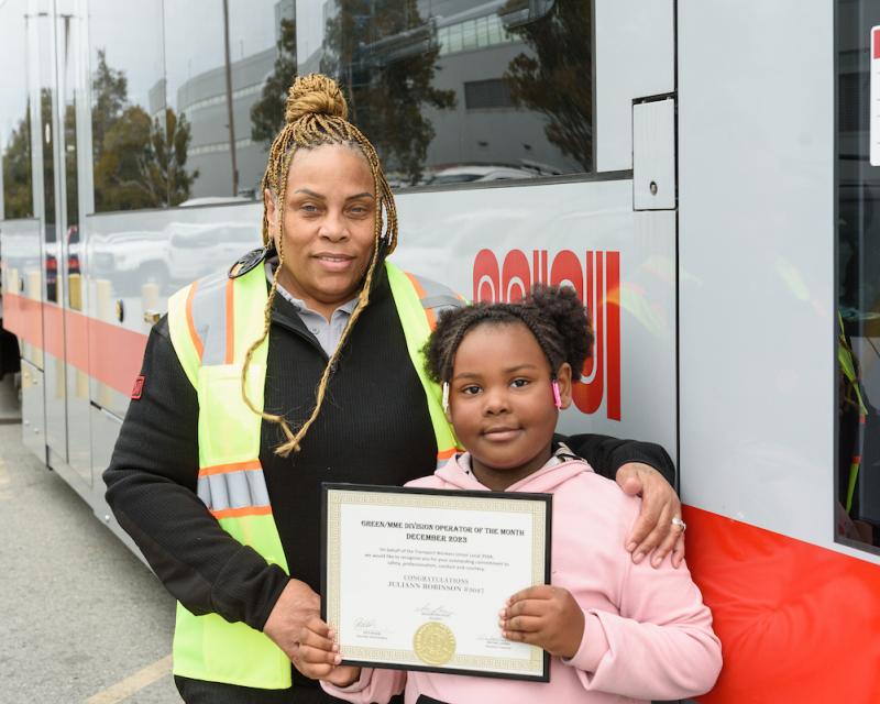 A woman and child standing in front of a train and holding a certificate.