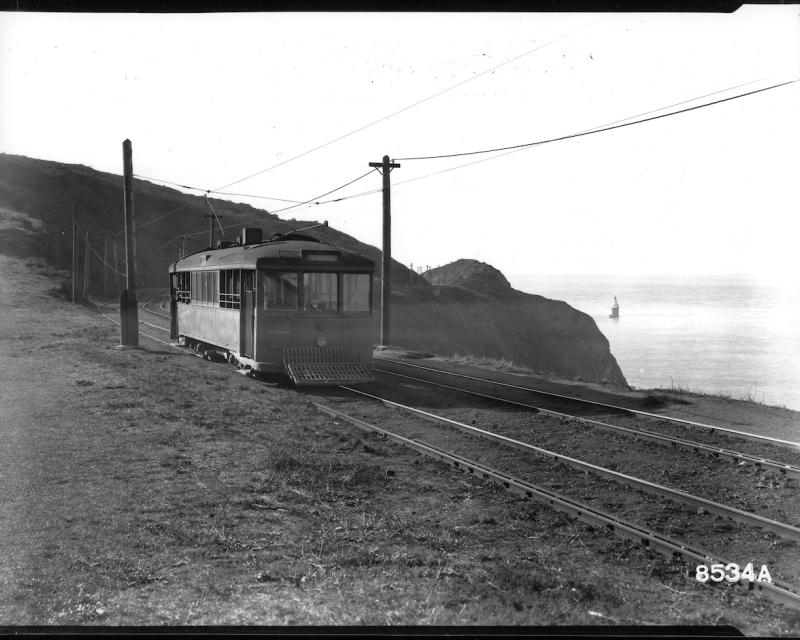 Black and white photo of a historic streetcar passing a cliff and waterway.