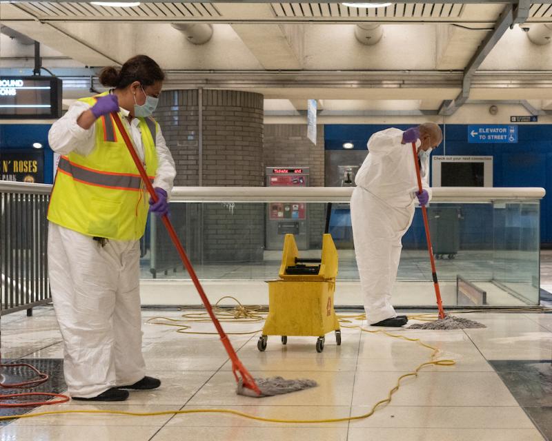 Two custodians clean the floor of a Muni platform.
