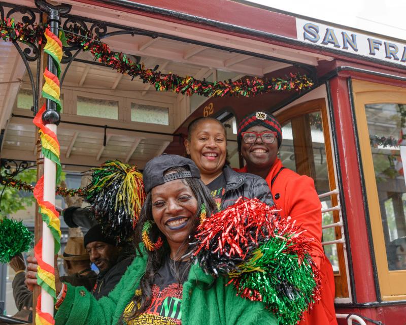 Three people smile from a motorized cable car that's decorated with Juneteenth colors during last year's parade.