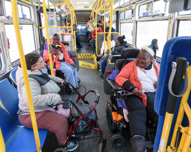 A person using a mobility device and a person using a walker interact in the front of a Muni bus.