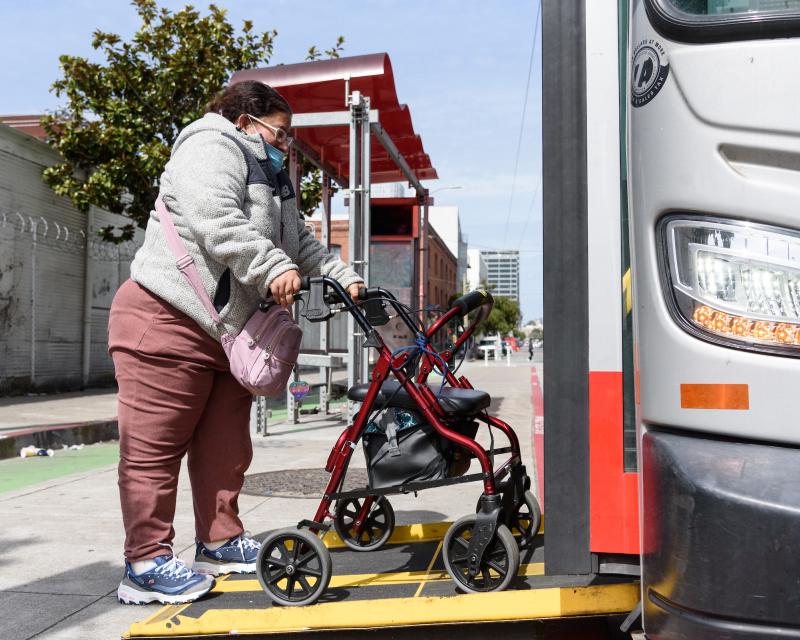 Person using a mobility device steps on a Muni ramp to enter a bus. 