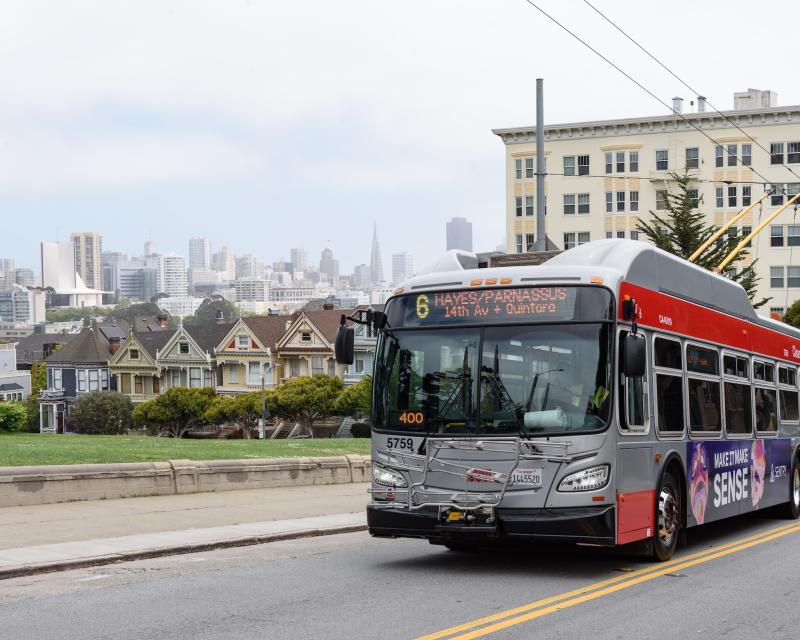 New 6 Hayes-Parnassus bus heads up a hill passing Alamo Square and the Painted Ladies houses.