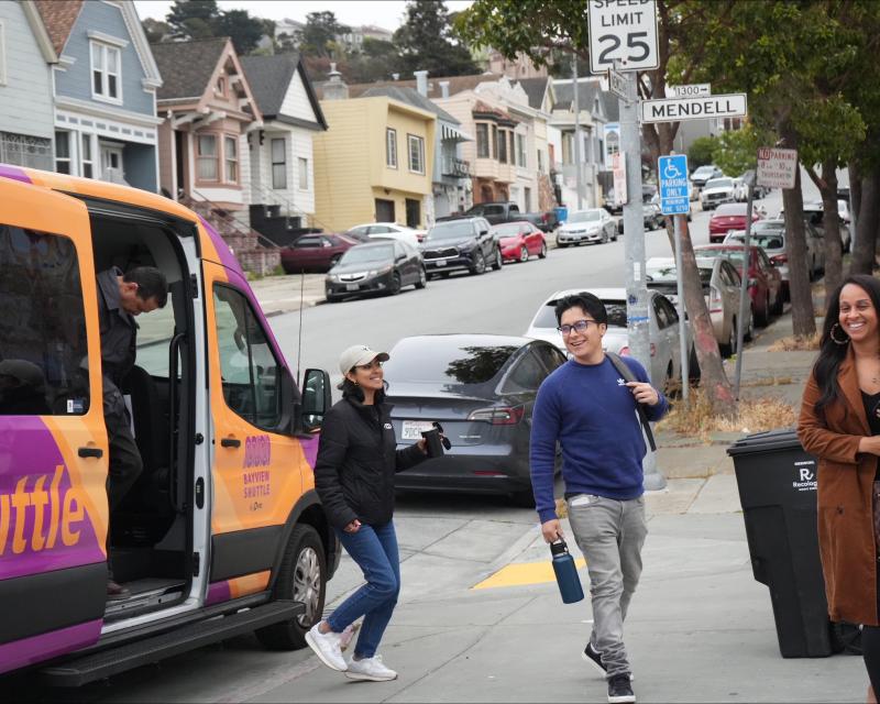 Three people exit an orange and purple Bayview Shuttle. 