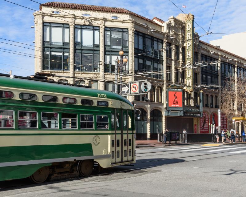 F Market streetcar that's green and cream heads downtown approaching the Orpheum Theatre.
