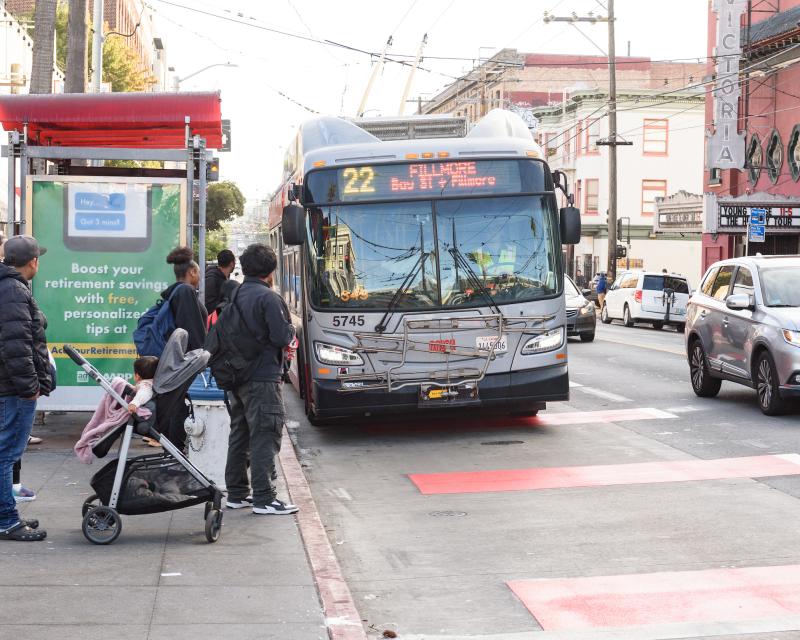 Several people wait to board a 22 Fillmore near a dedicated transit lane.
