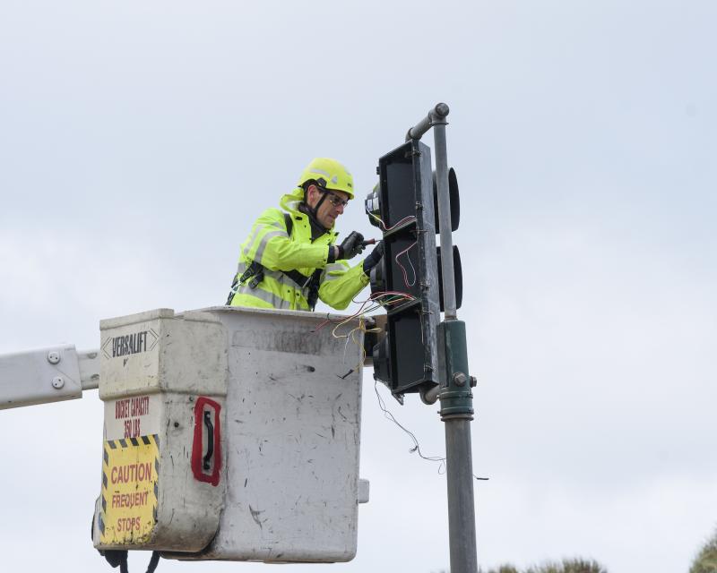 Person in a yellow vest and helmet installs a new traffic light in the Outer Sunset for the Great Highway road closure.