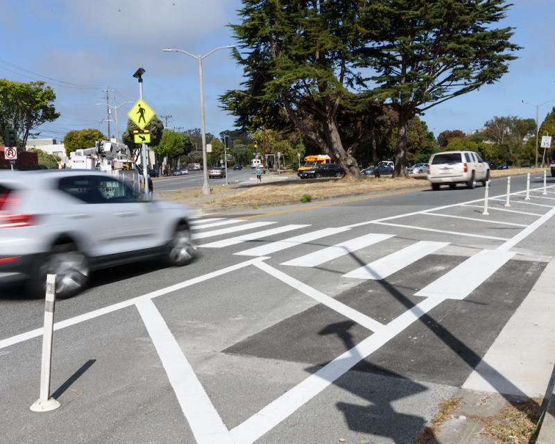 A crosswalk with an RRFB is depicted with two cars driving along the road