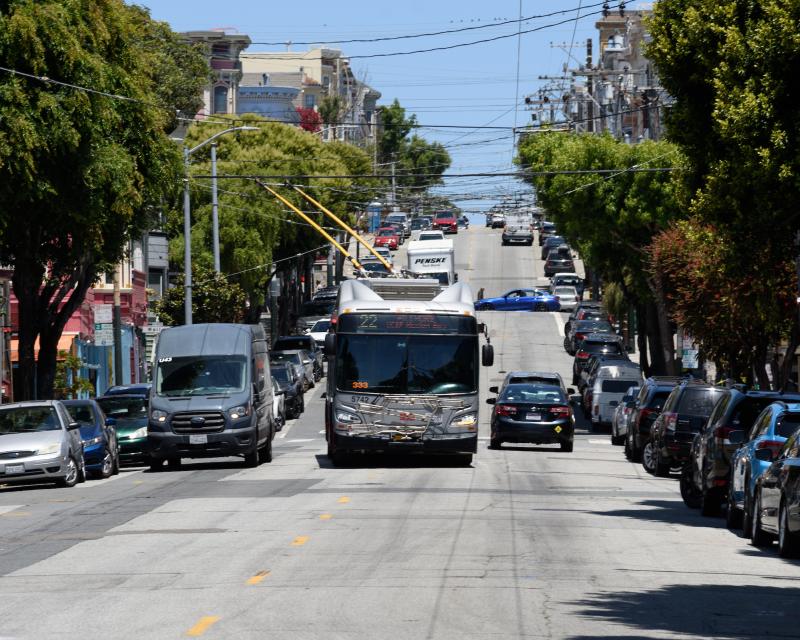 22 Fillmore bus drives around a double parked car on a city street.