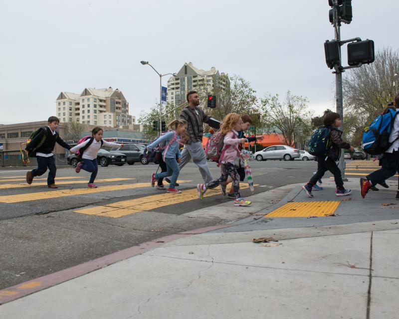 Several students and an adult cross a marked yellow crosswalk in San Francisco.