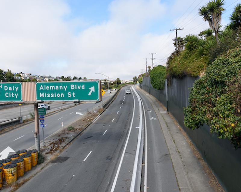 new protected bikeway on the Alemany blvd Mission street exit ramp, concrete k-rail barriers separate the bike lane from the vehicle lanes. 