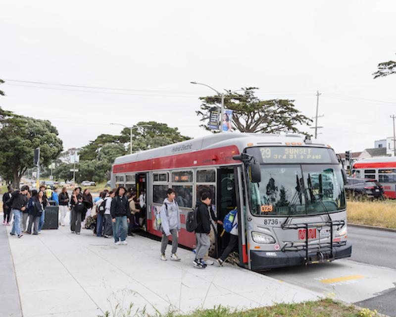 Several students board a 29 Sunset from a paved concrete stop.