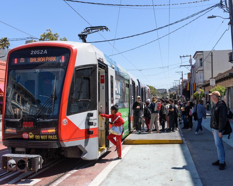 People board a train near a curb. 
