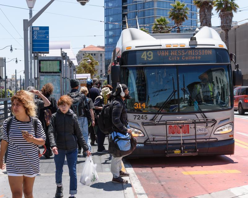People boarding and exiting a 49 Van Ness bus parked in a dedicated transit lane.