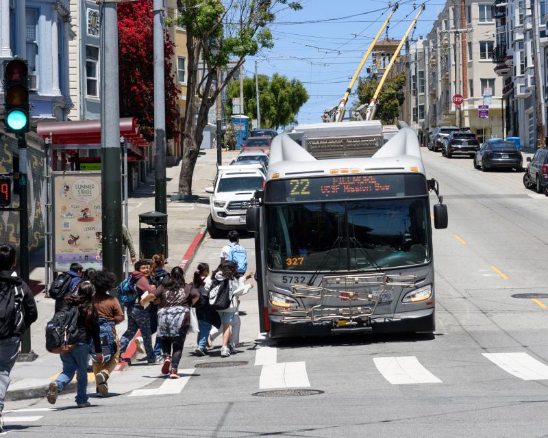 Several people walk to a 22 Fillmore stop to board a bus.