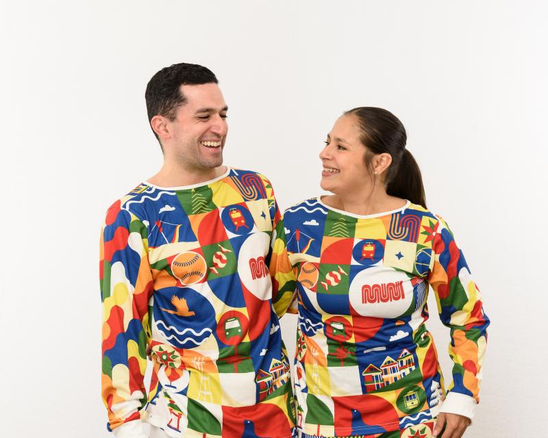Two people laugh and smile as they pose in Merry Days of Muni Holiday Pajama Sets.
