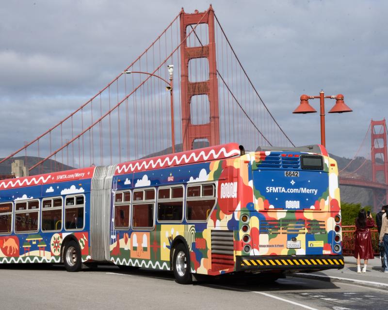 Bus wrapped with Merry Days of Muni stops in front of the Golden Gate Bridge.