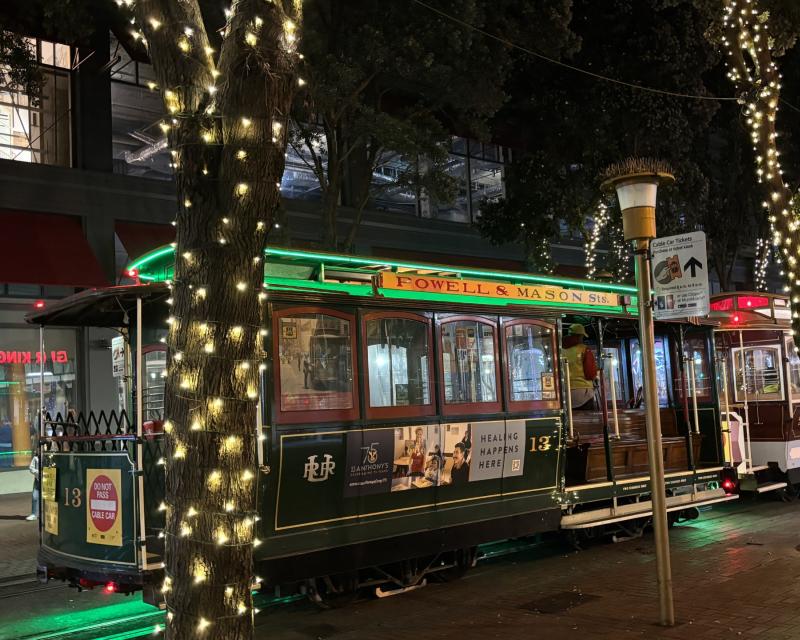 A cable car parked behind trees decorated with lights.