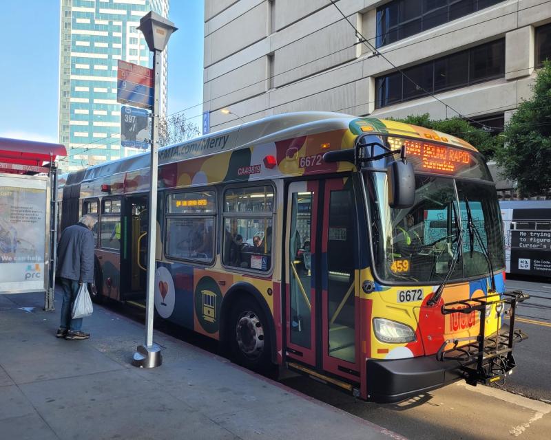 A 9R San Bruno with a Merry Days of Muni wrap stops to pick up a passenger.