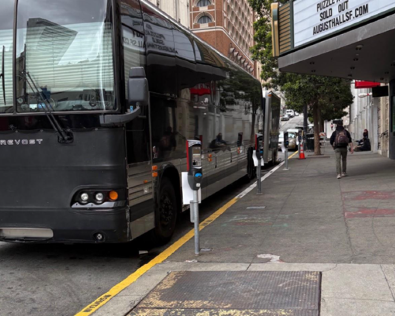 A black shuttle bus is parked outside of an entertainment venue.