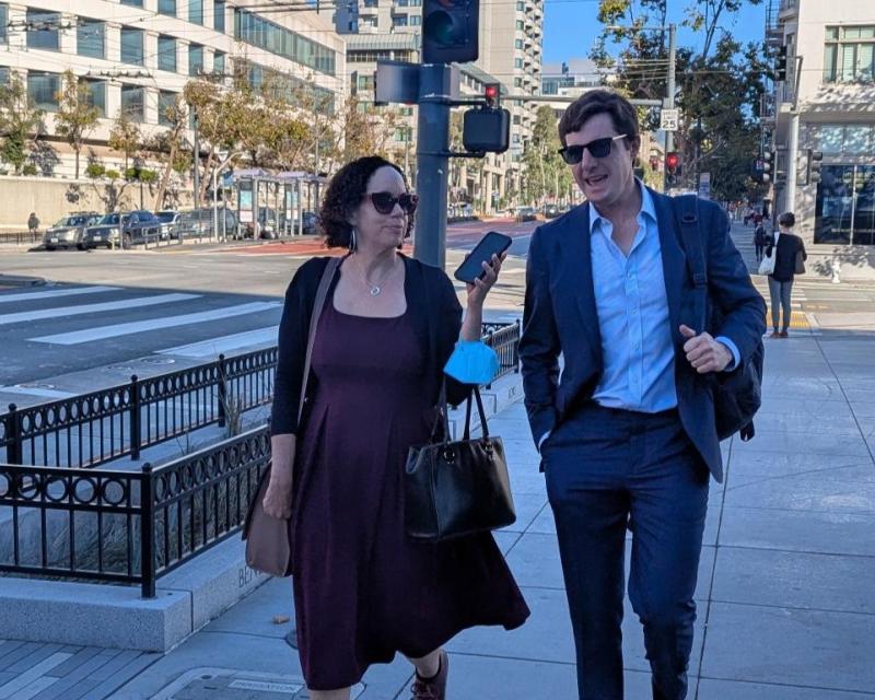 Two people walking on the sidewalk and talking.