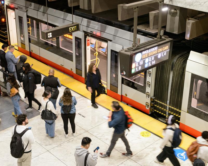 People wait for trains and exit trains on a Muni Metro platform.