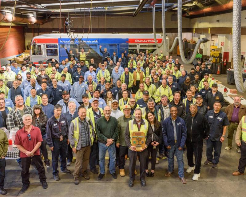 Large group of SFMTA staff in a bus yard. Many wear yellow vests.