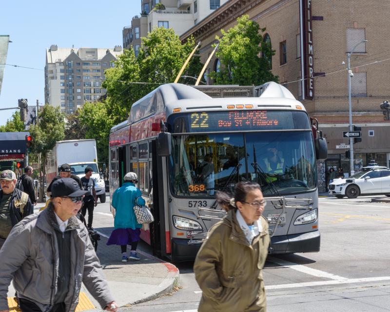a 22 Fillmore trolley bus waits at a stop, people are walking away from the bus stop, while others board the bus