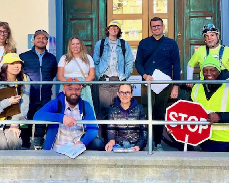 School staff, parents and community members smile for a photo in front of a school ahead of a school walk audit.
