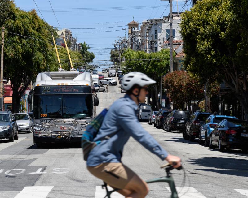 Person riding a bike with the 22 Fillmore bus in the background. 