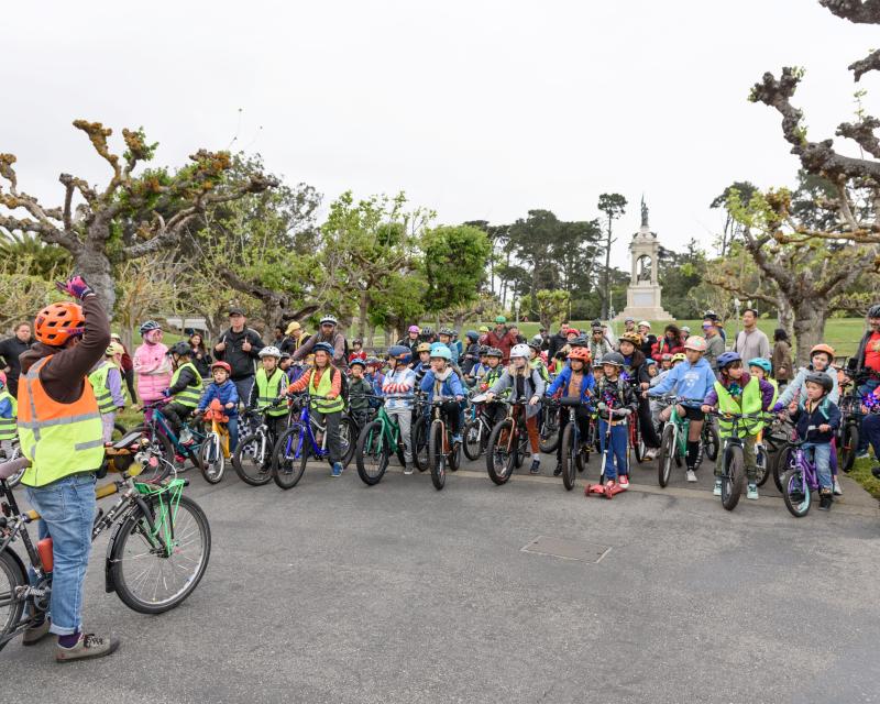 Kids and adults on bikes in front of trees.