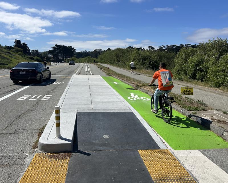 person on bike riding in new bike lane on Lake Merced Blvd next to a new transit boarding island