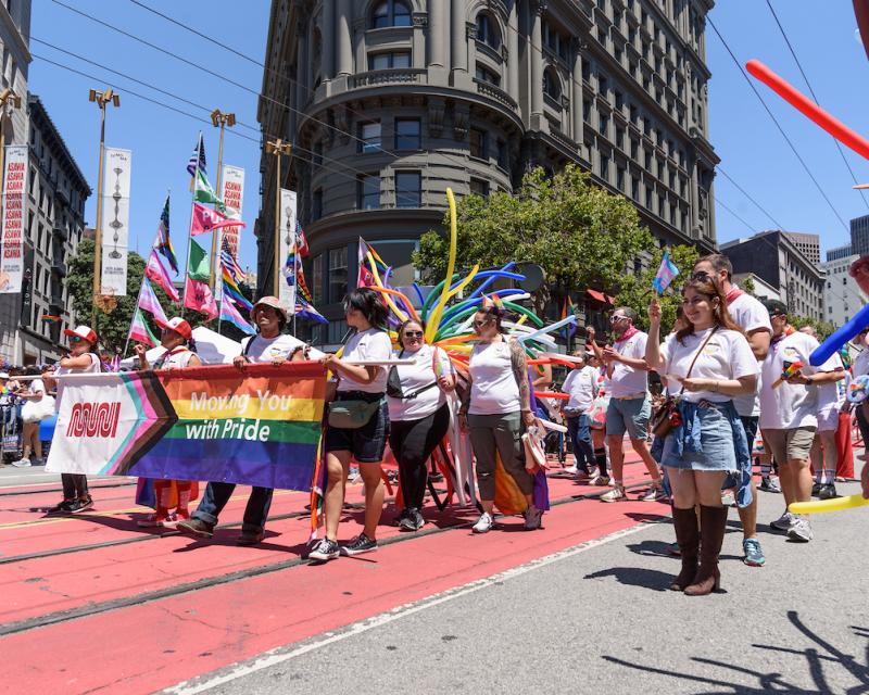 SFMTA staff marching on Market Street with a banner says “Moving you with Pride” at the San Francisco Pride Parade.