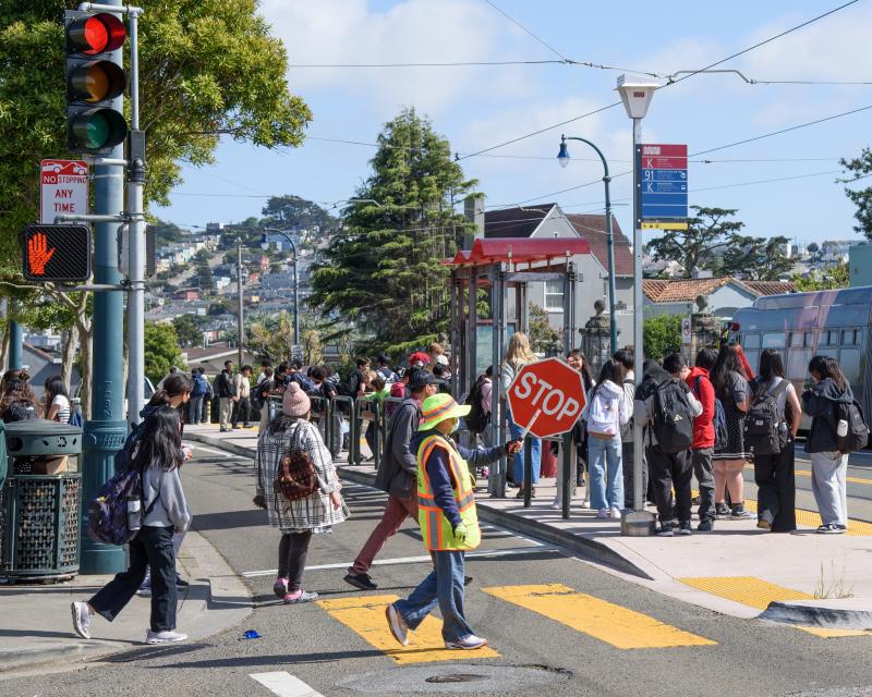 People walking through a crosswalk and waiting at a bus stop.