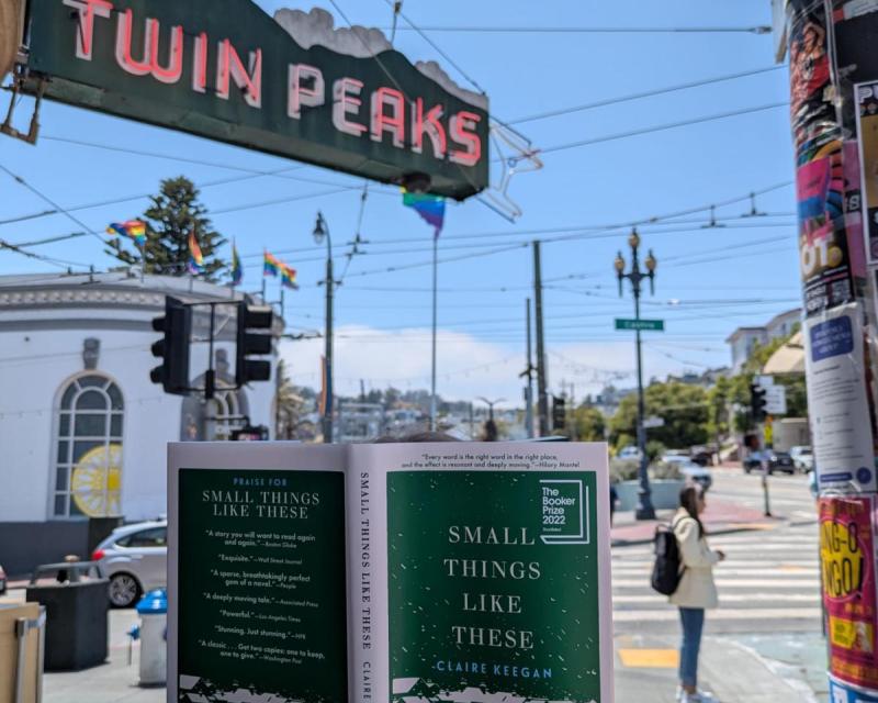  A person holds a copy of Claire Keegan’s “Small Things Like These” in front of the Castro street sign and Twin Peaks Tavern on a sunny day in San Francisco. 