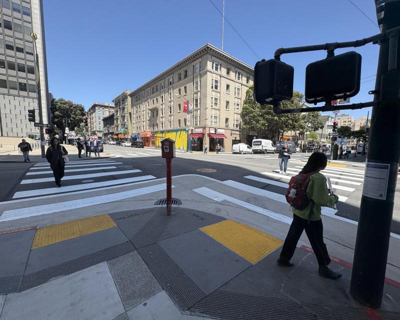 Pedestrians using new crosswalk at Larkin and Golden Gate intersection. One person waits near the traffic signal near the yellow tactile domes in the curb ramp leading to the crosswalk.